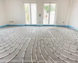 Instalación de tuberías para suelo radiante en una habitación en construcción. Las tuberías blancas forman un patrón curvo sobre una malla gris.