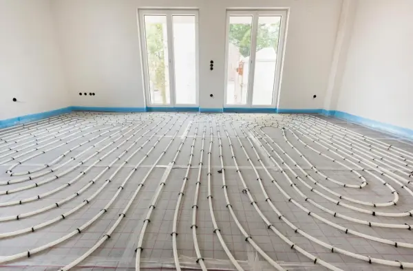 Instalación de tuberías para suelo radiante en una habitación en construcción. Las tuberías blancas forman un patrón curvo sobre una malla gris.