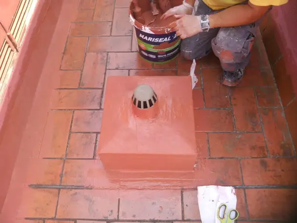 Persona aplica pintura para impermeabilizar terraza. Cubeta de Mariseal y desagüe en el centro.