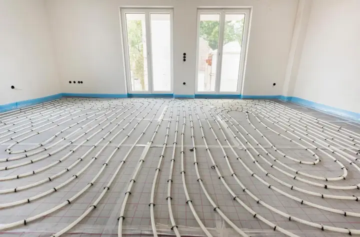 Instalación de tuberías para suelo radiante en una habitación en construcción. Las tuberías blancas forman un patrón curvo sobre una malla gris.